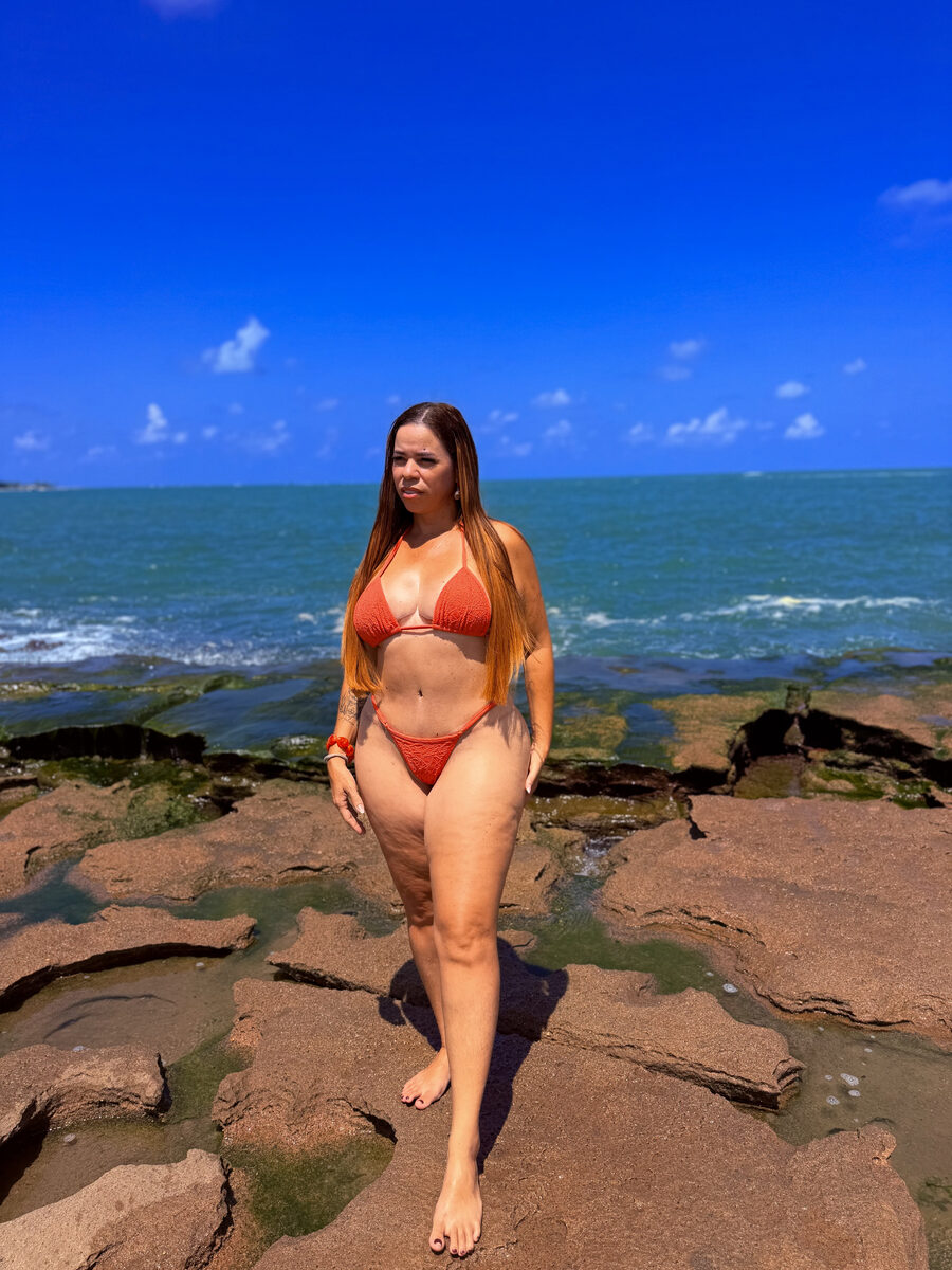 Greice de biquíni laranja sobre as pedras do mar