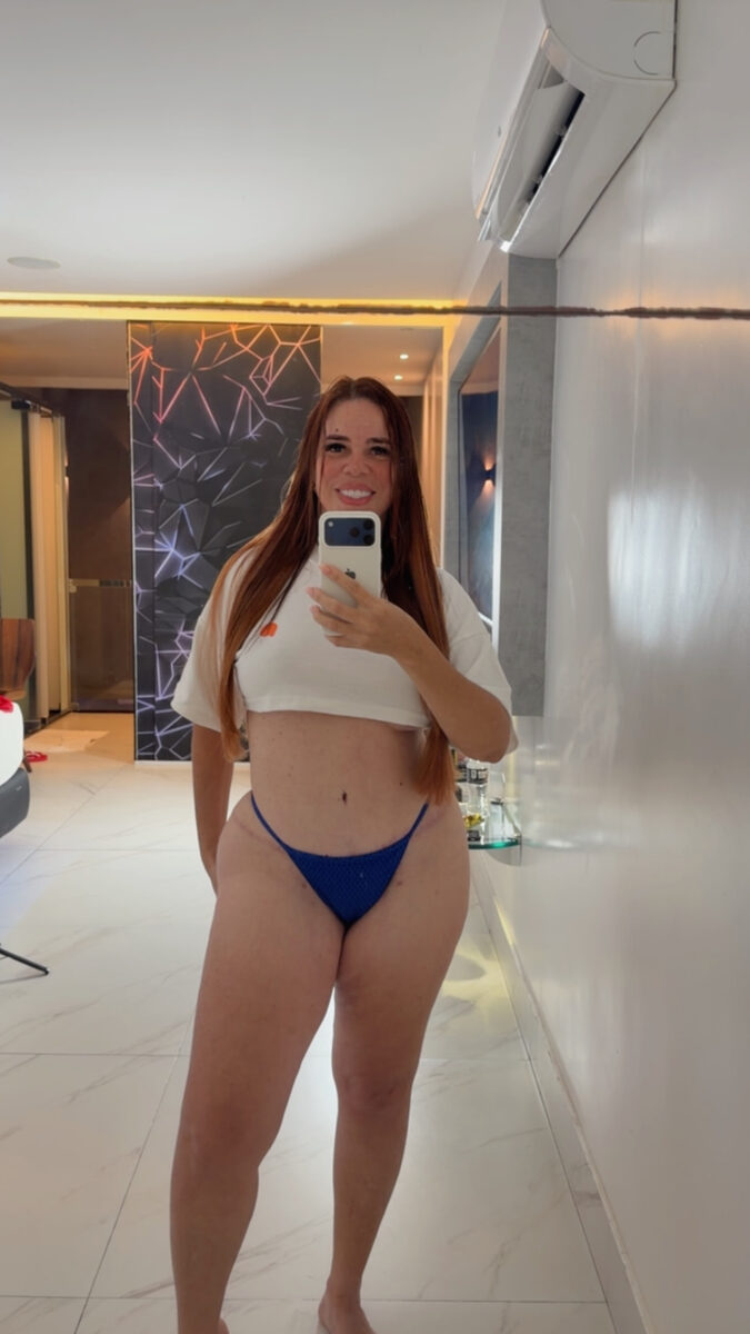 Greice sorrindo no espelho, de top branco